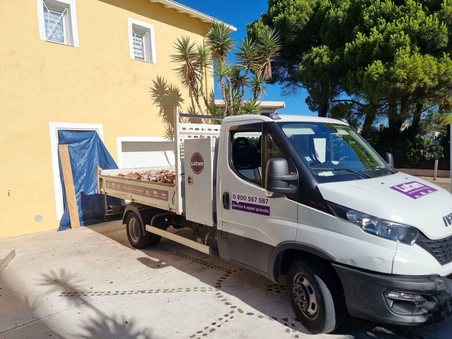 Camion benne chargé de tuiles devant une maison individuelle en cours de rénovation